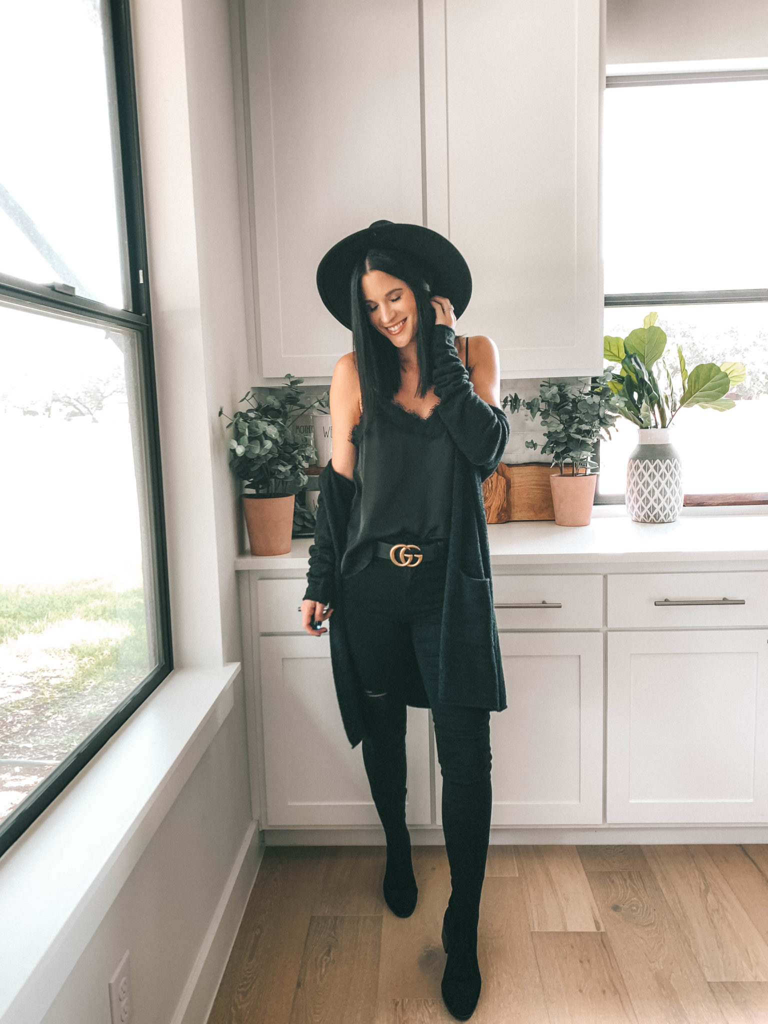 How to Style an All Black Outfit 3 Different Ways by popular Austin blog, Dressed to Kill: image of woman standing in her kitchen and wearing a black Articles of Society Sarah Skinny Ankle Jeans, black Lace Trim Satin Camisole Top, and black Barefoot Dreams CozyChic Lite® Circle Cardigan.  