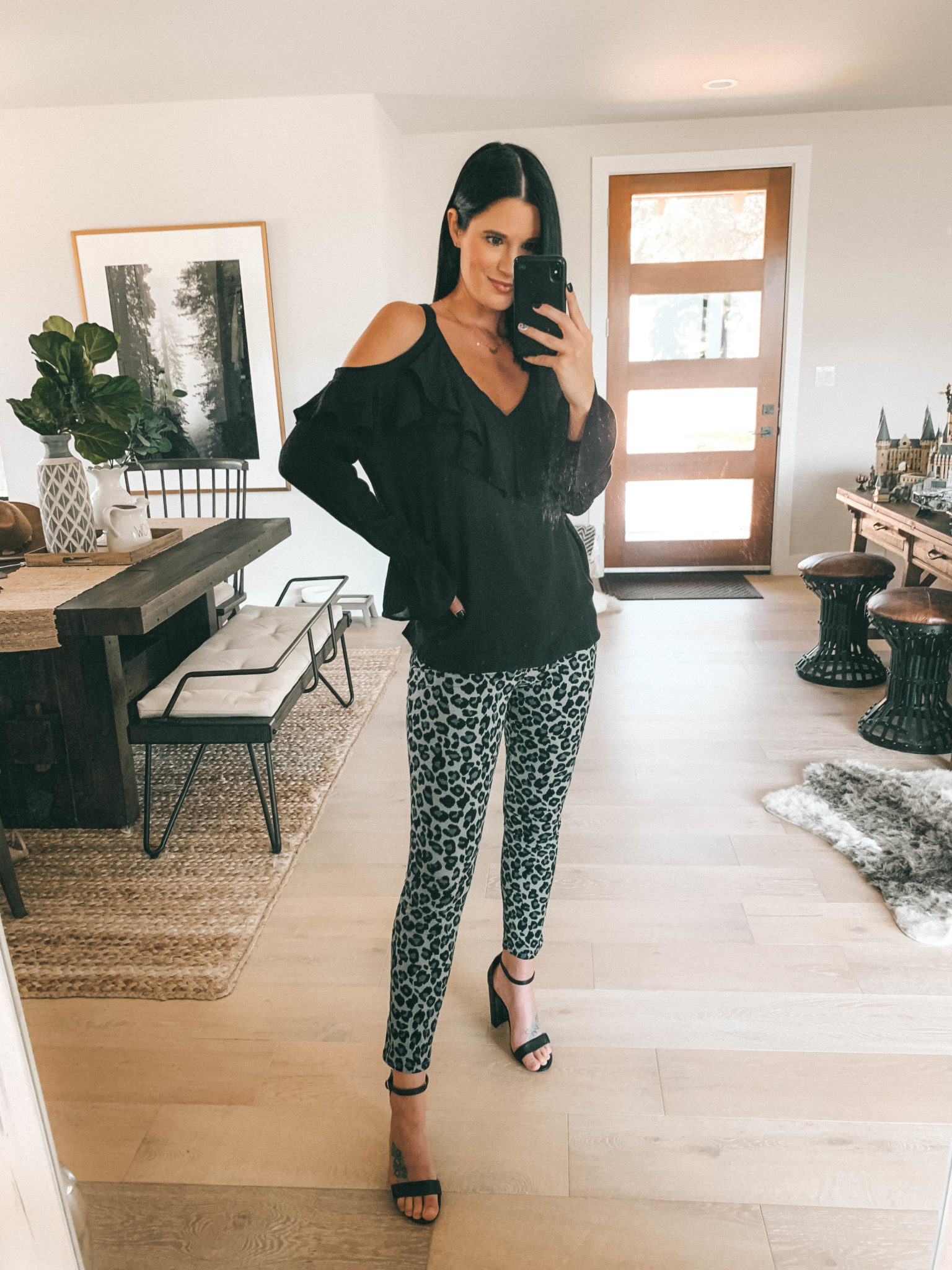 7 Affordable Fall Outfits from Walmart by popular Austin fashion blog, Dressed to Kill: image of a woman standing inside her house and wearing a black Walmart Sofia Jeans Cold-Shoulder Ruffle Neck Woven Top and Sofia Jeans Sofia Skinny Leopard Print Mid Rise Stretch Ankle Jean.