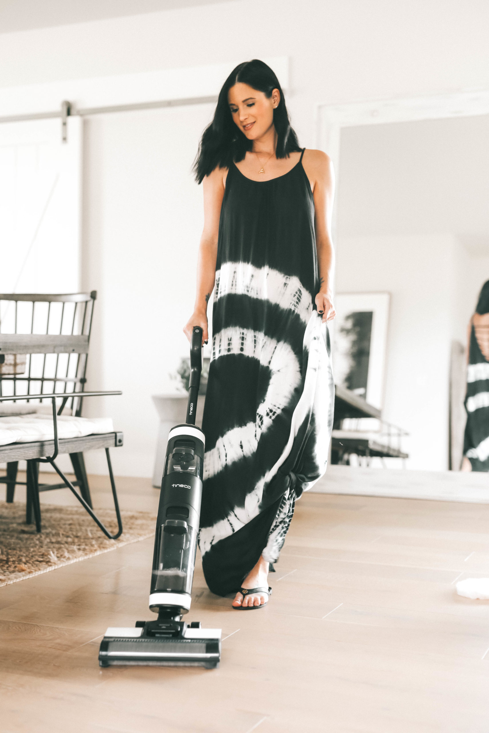 Tineco Floor One S3 by popular Austin lifestyle blog, Dressed to Kill: image of a woman wearing a black and white tie dye maxi and using a Tineco Floor One S3 vacuum in her kitchen. 