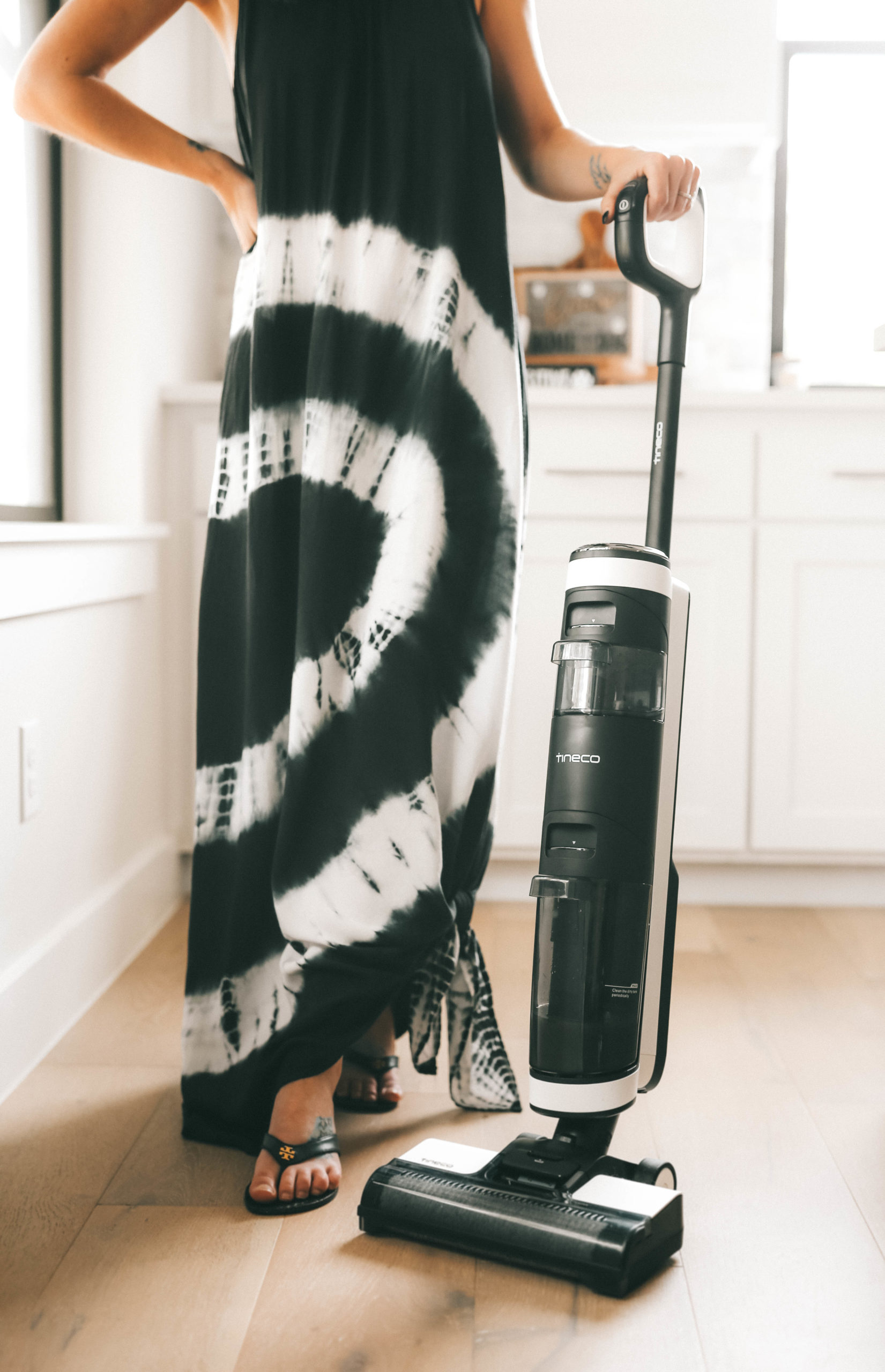 Tineco Floor One S3 by popular Austin lifestyle blog, Dressed to Kill: image of a woman wearing a black and white tie dye maxi and standing in her kitchen next to a Tineco Floor One S3 vacuum. 